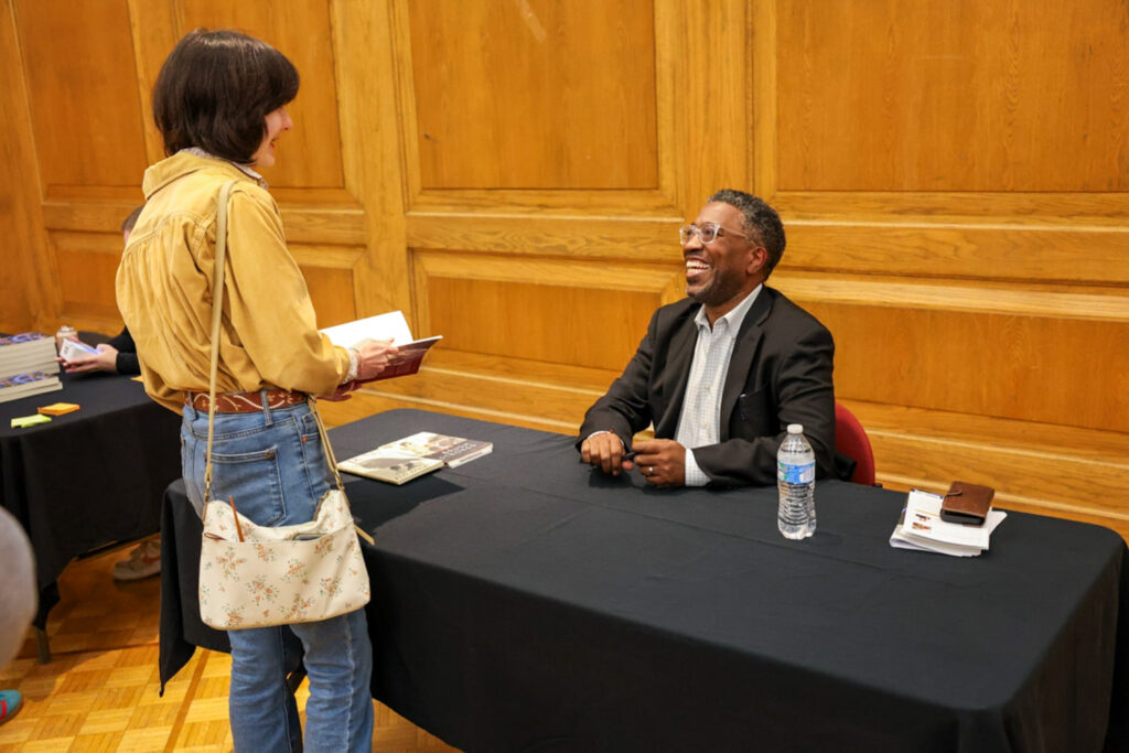 Major Jackson sits at a table smiling up at a person holding his book.