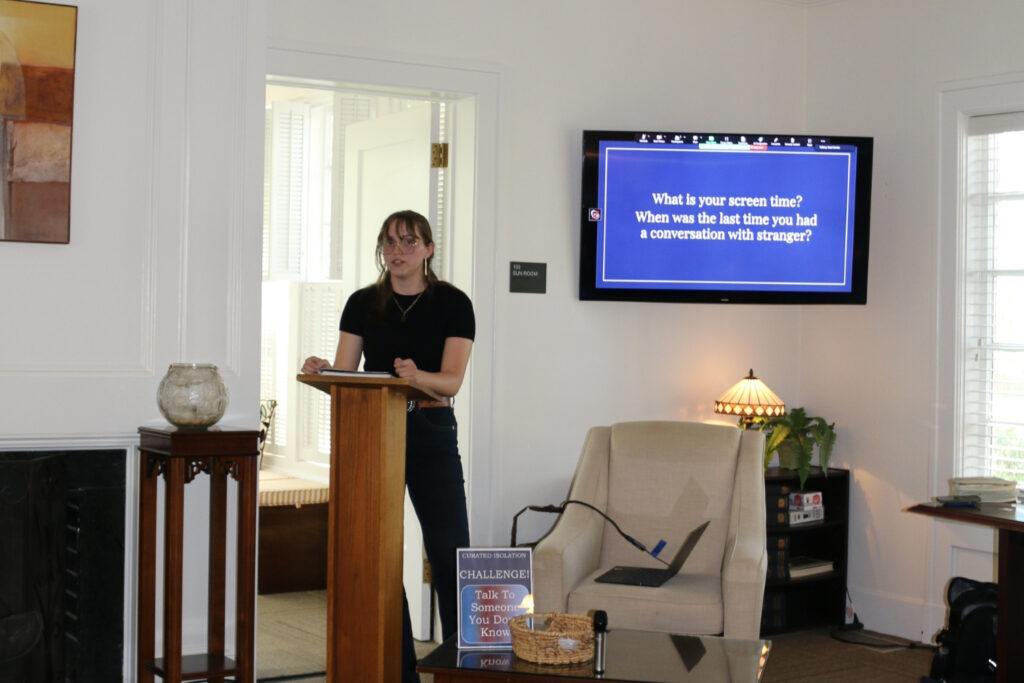 One person stands at a podium in front of a tv in a dimly lit room.
