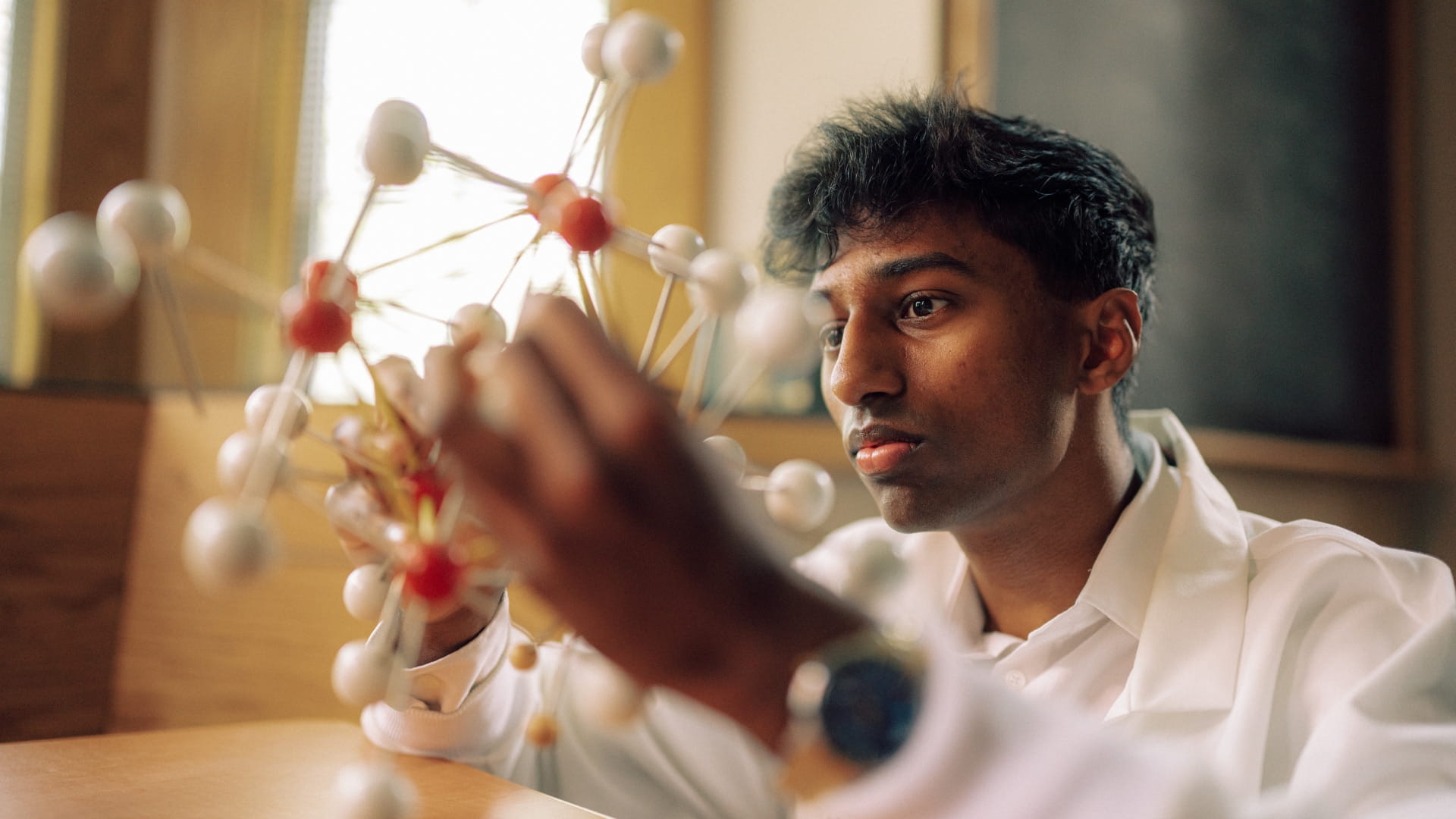 One Hendrix student in a white lab coat holding a molecular model in front of them.