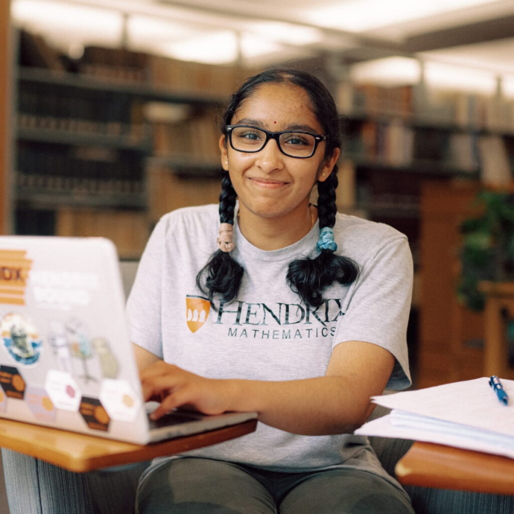 A Hendrix student smiles as she sits in the library working on her laptop.