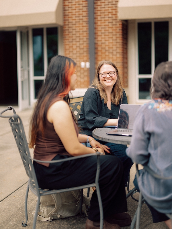 Student meets with faculty and career advisors outdoors while reviewing work on laptops.