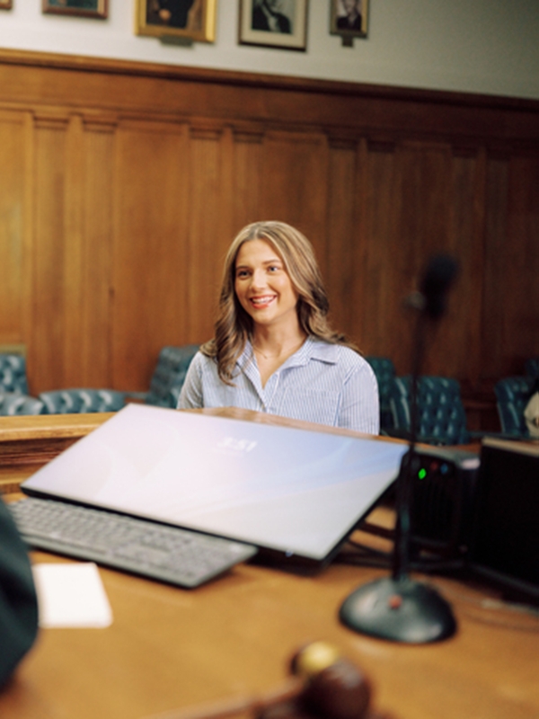 Smiling student stands near judge's bench in a courtroom.
