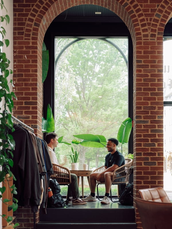 Two students sit at a table, talking over coffee in a campus gathering space.