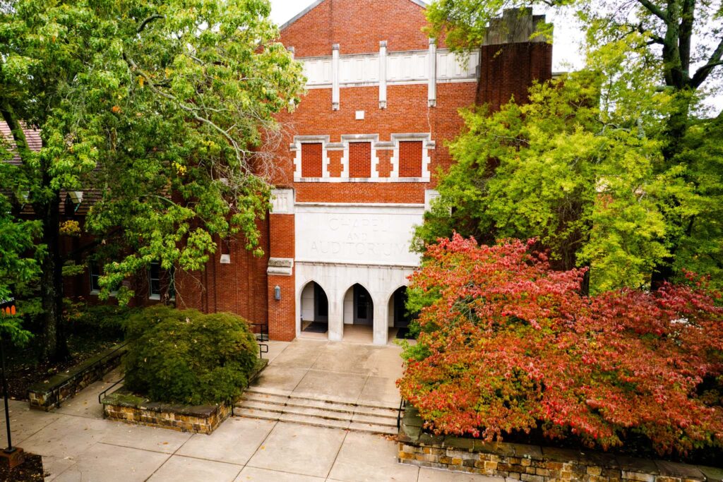 Exterior of brick and stone building on campus with trees turning colors in the fall.