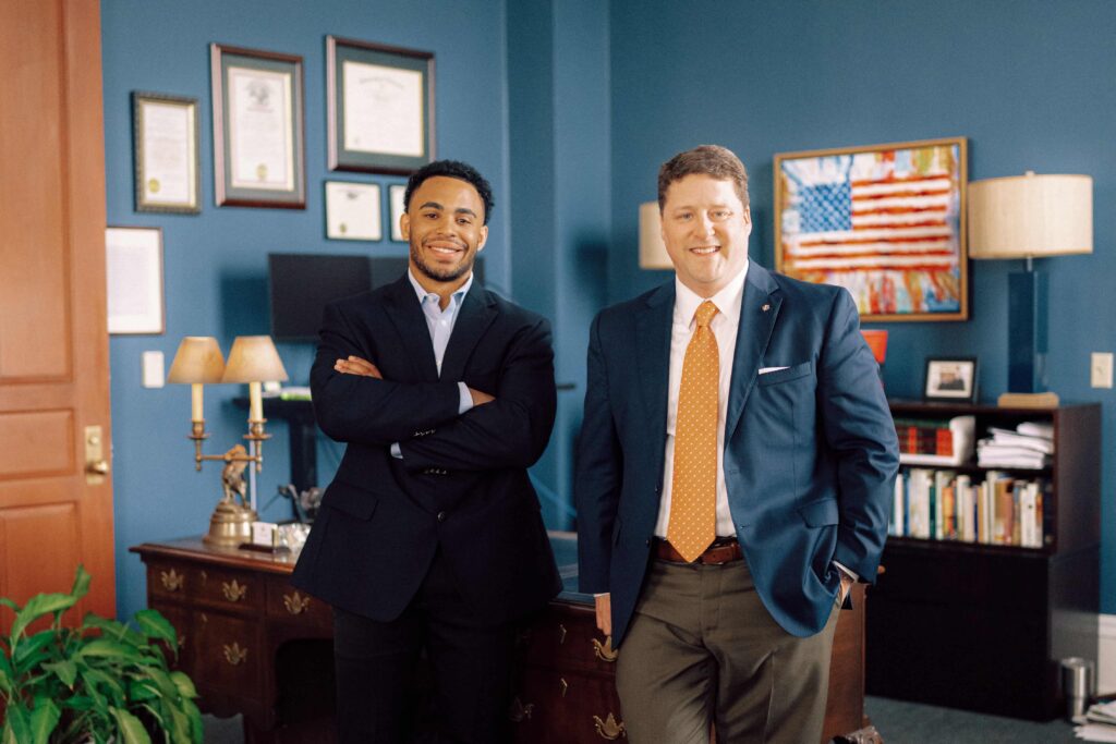 Two mean in suits standing in front of a wooden desk in an office.