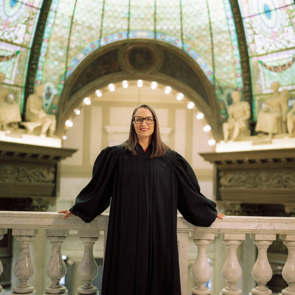 A woman wearing a black robe standing by a marble railing inside a rotunda.