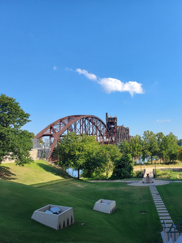A park with pathways, and a metal bridge in the background.