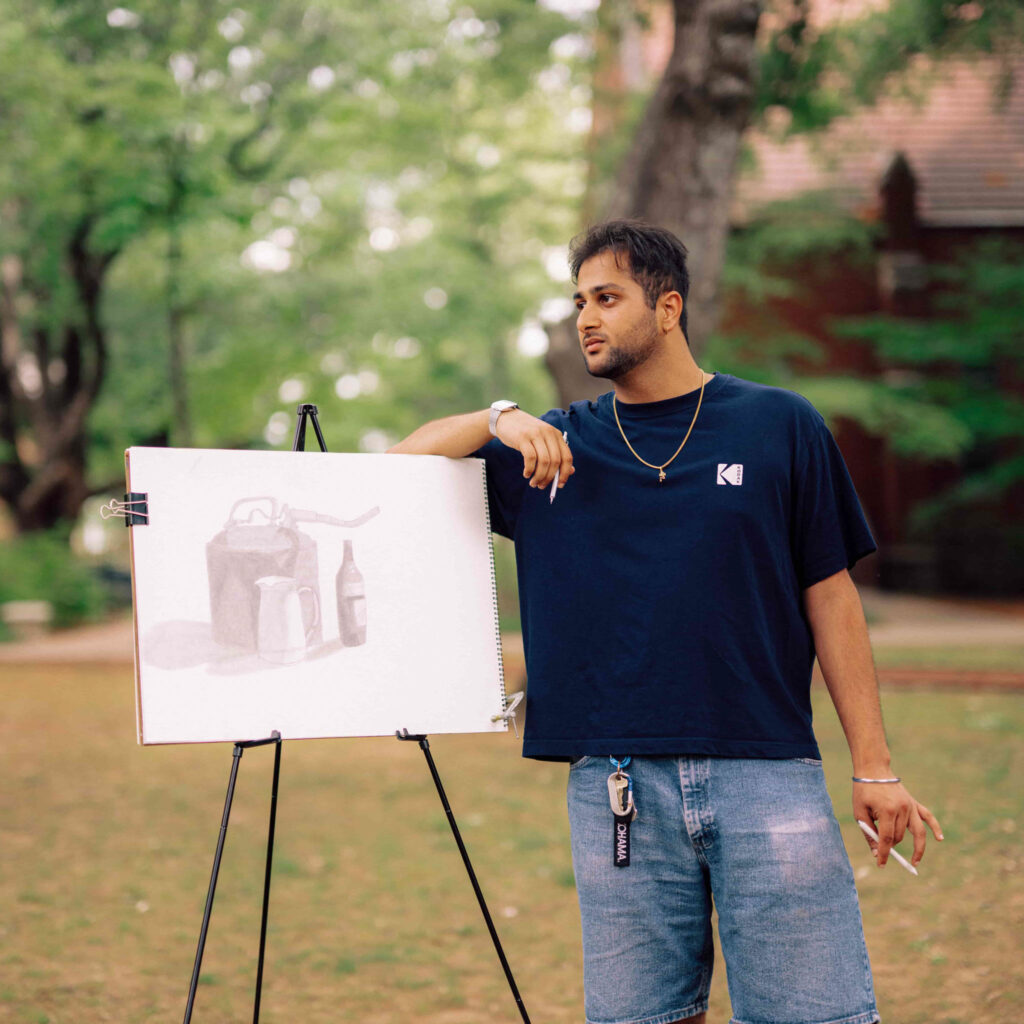 A student working on a still life sketch that is resting on an easel outdoors.