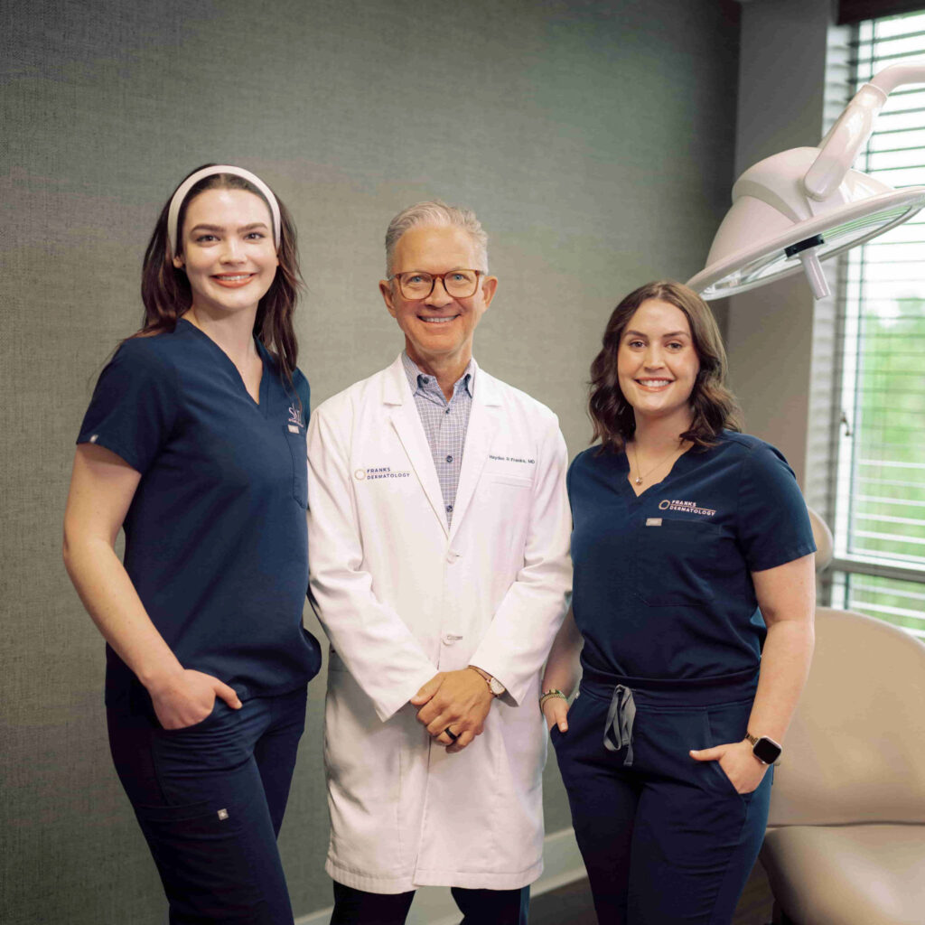 Two Hendrix students in scrubs standing with a doctor in a patient exam room.