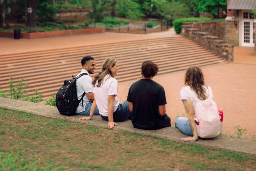 Four Hendrix students sitting on a stone wall, talking to each other.