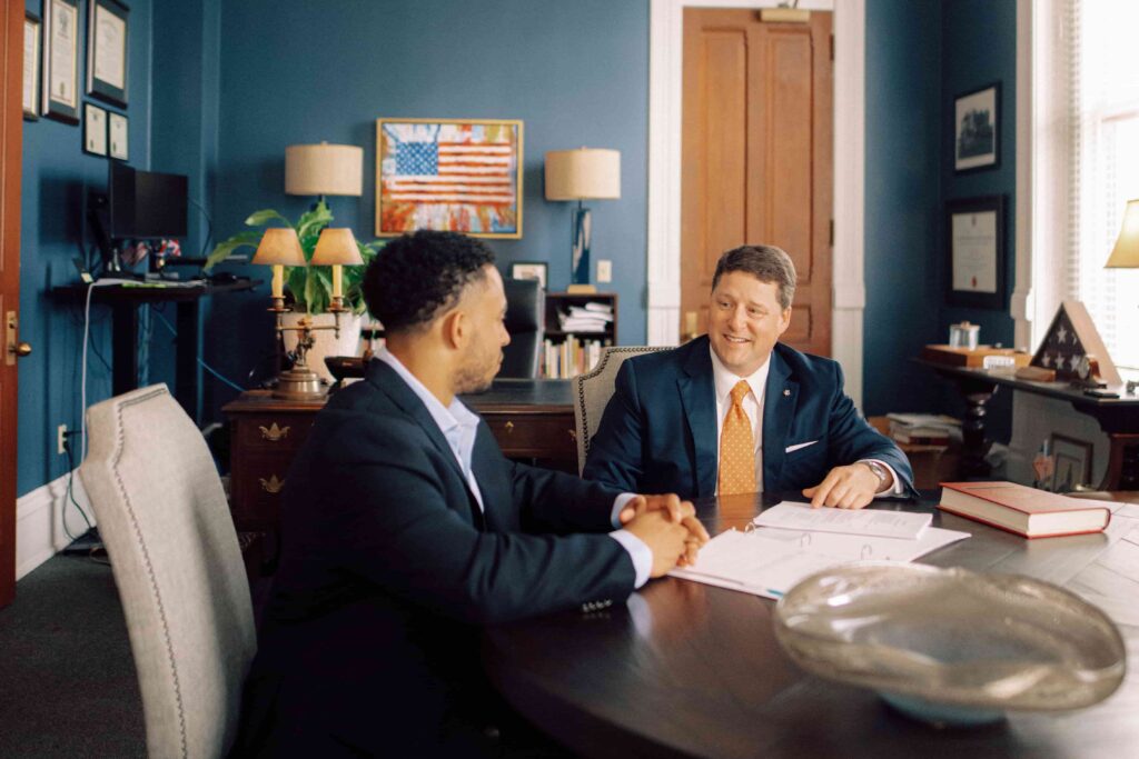 Two men in suits sitting at a table reviewing paperwork.