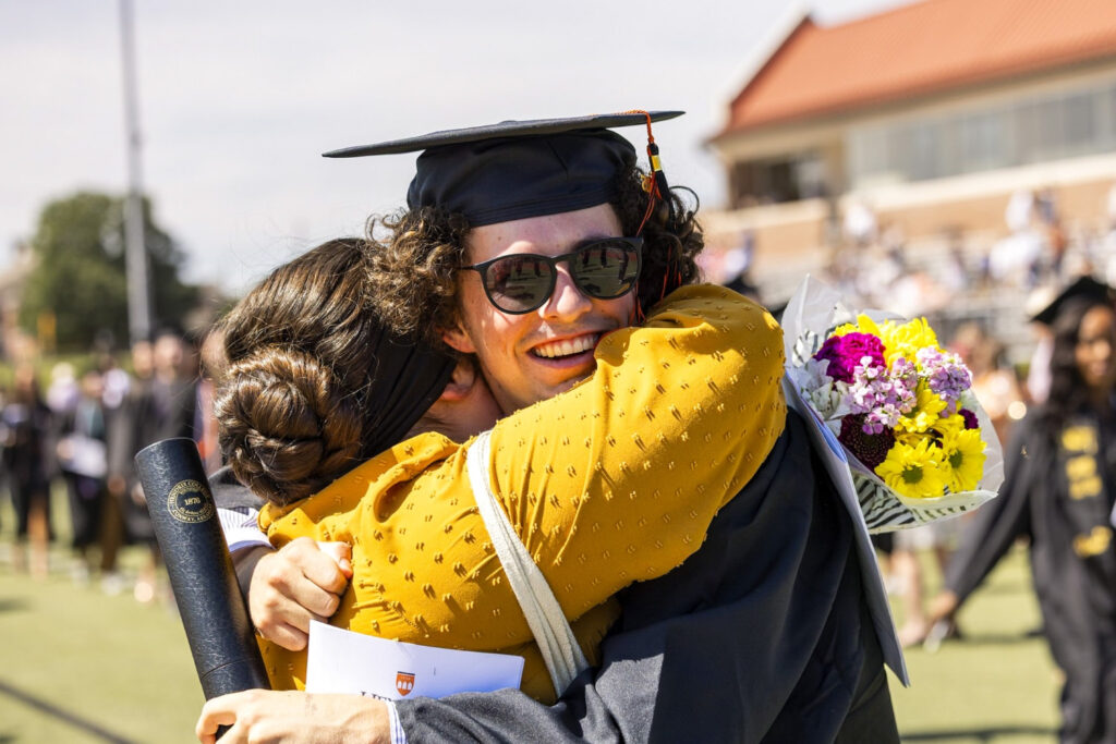 Two people hugging at a Hendrix Graduation Commencement outside on a sunny day.