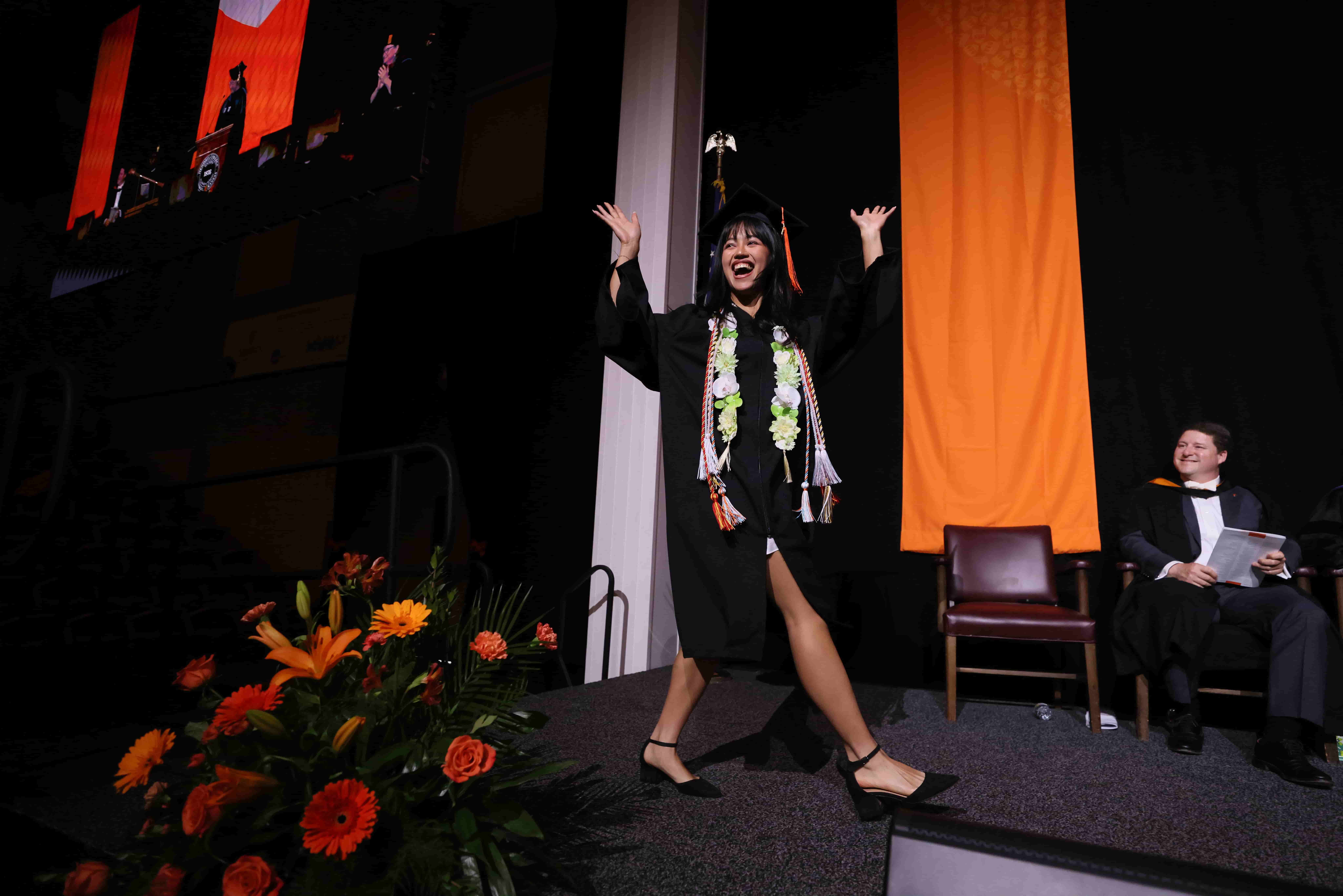 A student walking across the stage in cap and gown during commencement.