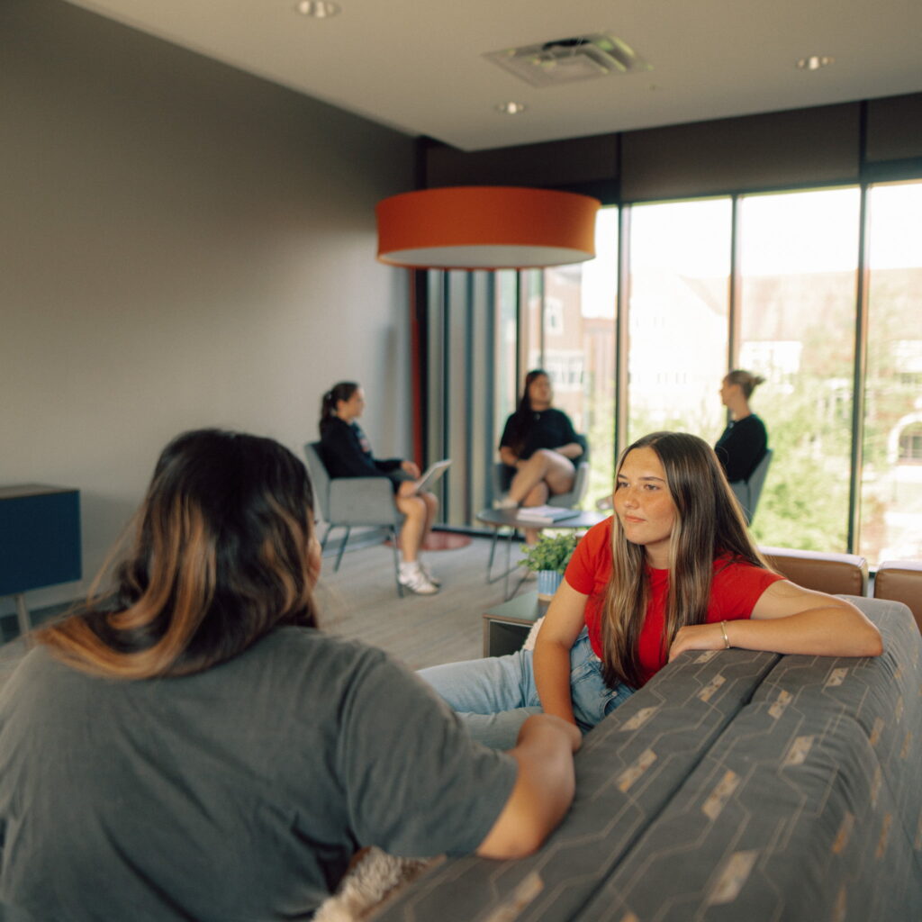 Groups of students sitting in a student lounge area having conversations.