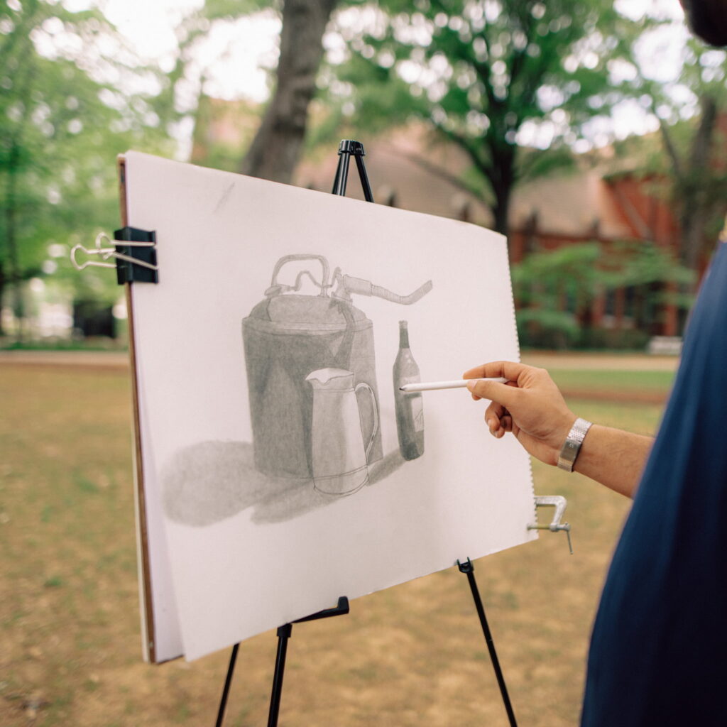 A student working on a still life sketch on an easel outdoors.