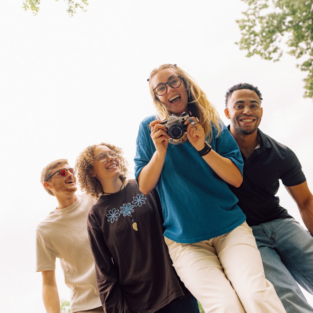 A group of four smiling Hendrix students. The student in front is holding a camera.