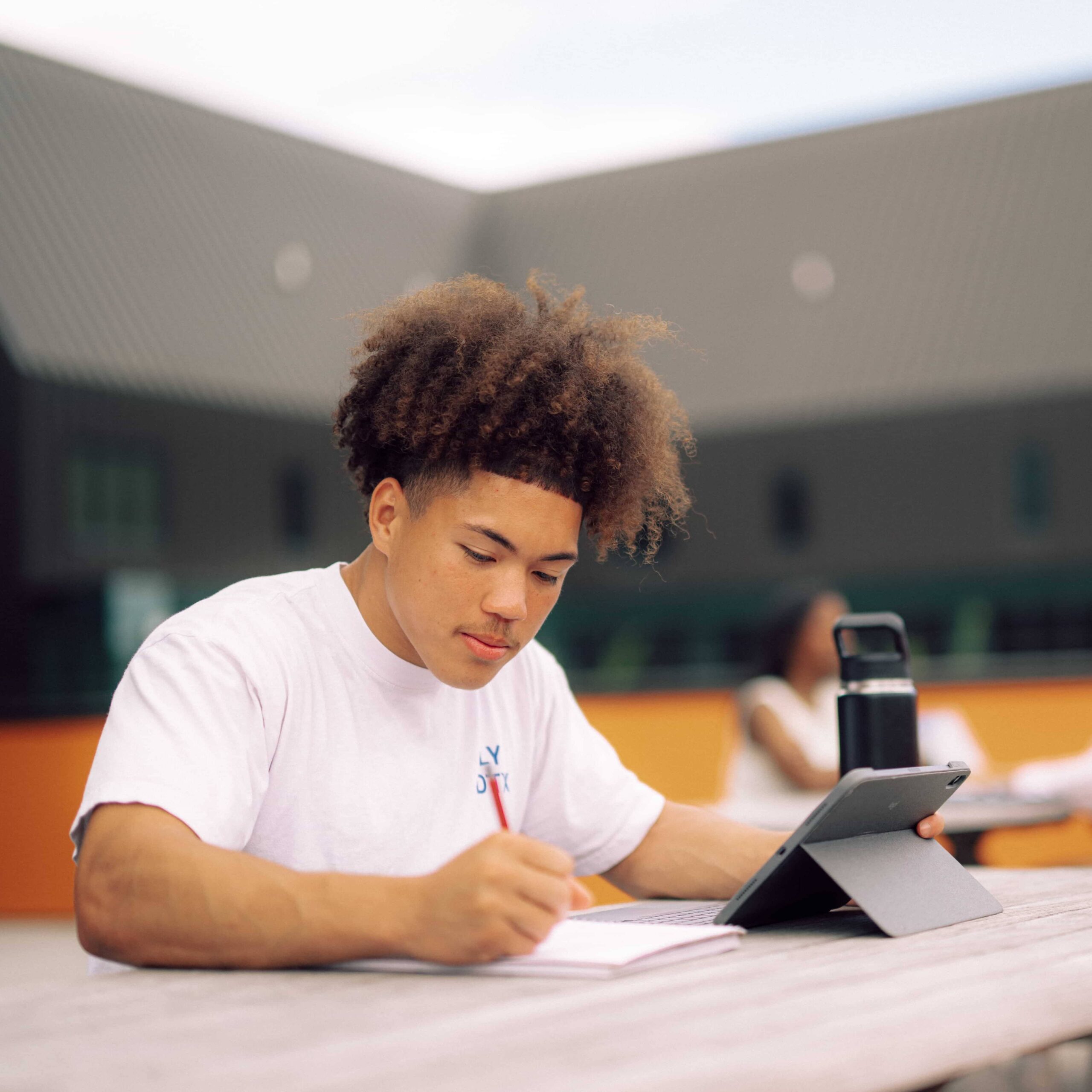 A male student studying with a tablet, a bottle of water, and a notebook.