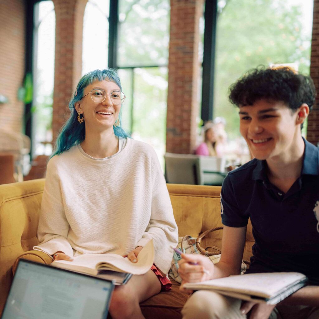 Two smiling students studying in a lounge space.