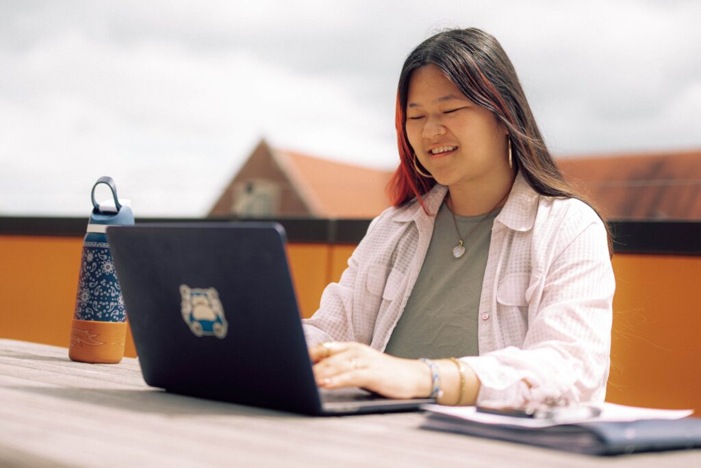 A student using a laptop while sitting in a rooftop lounge space.
