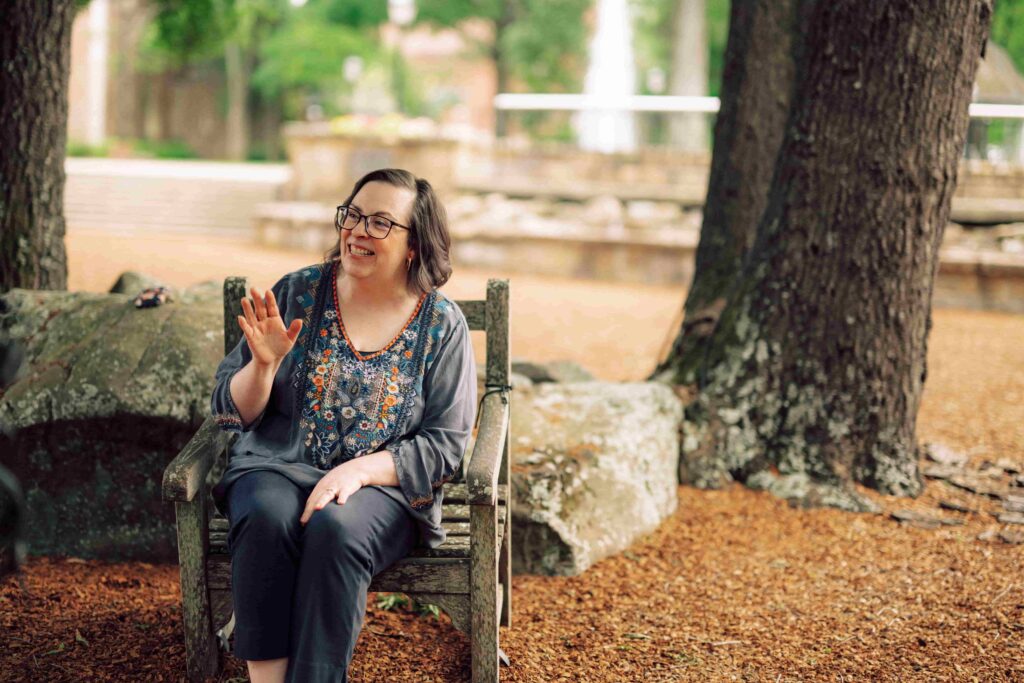 A Hendrix faculty member sitting in a wooden chair outdoors on campus.