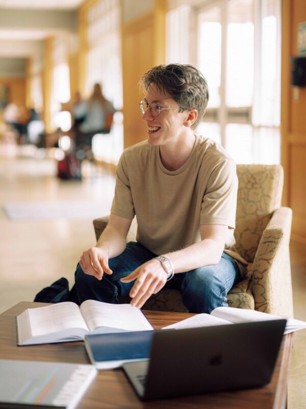 A student with open books and a laptop computer studying in an indoor lobby space.