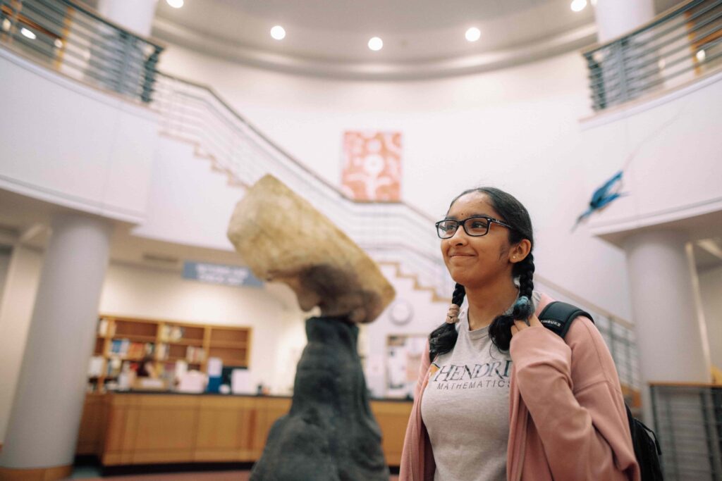 Hendrix student standing in the lobby of a building on campus, with a backpack over her shoulder.