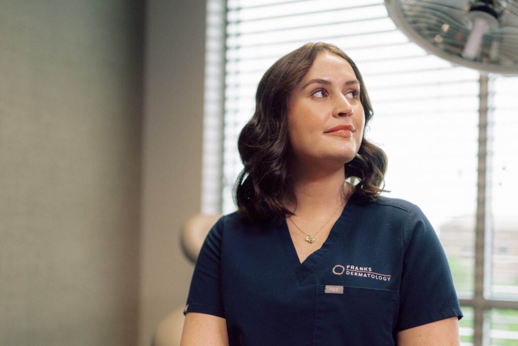 A female student wearing scrubs sitting in a patient exam room.