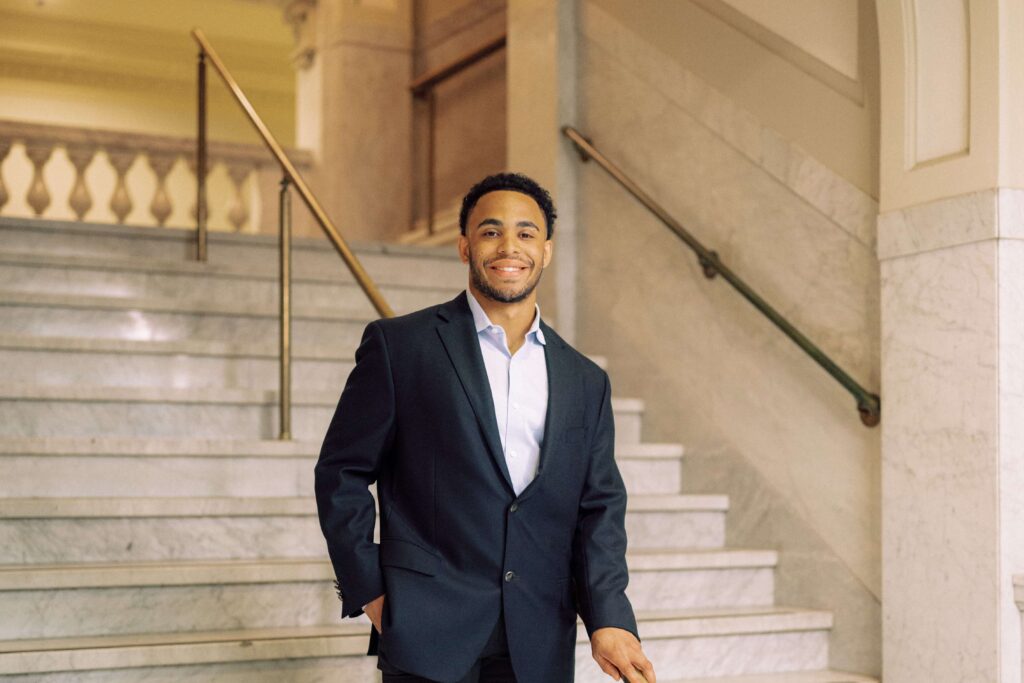 A male student in a suit standing on stone steps inside a building.