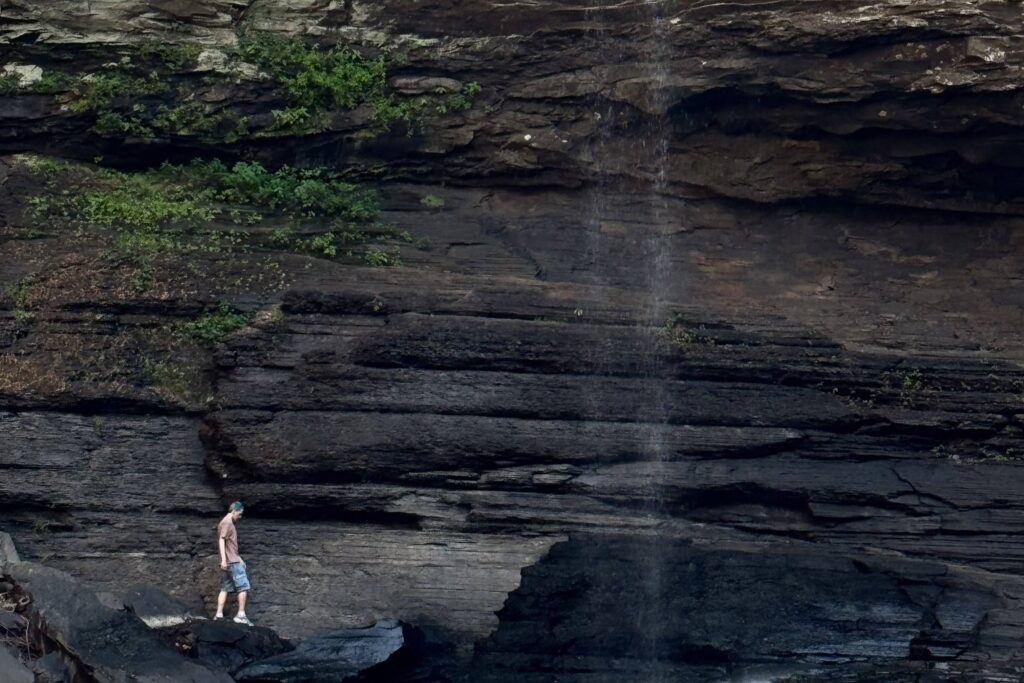 A student walking next to a cliff, approaching a waterfall.