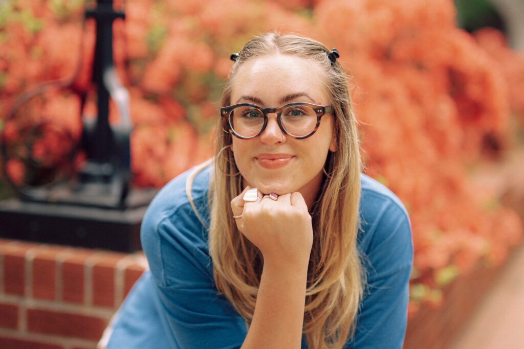 A student sitting in front of a bed of flowers, smiling at the camera.