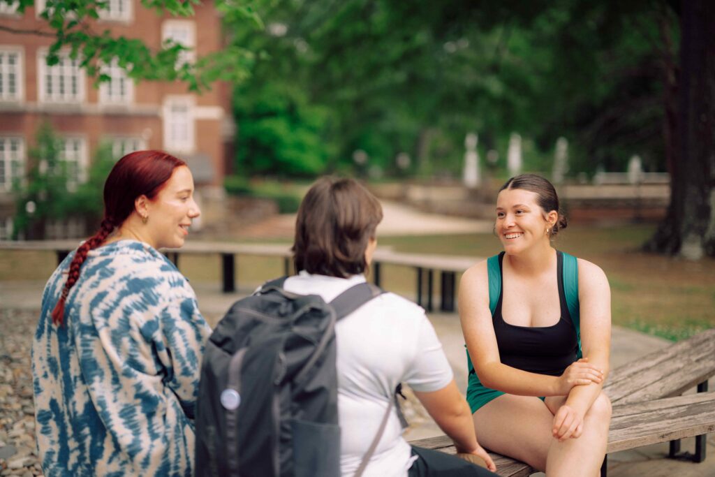 Three students sitting on outdoor benches having a conversation.