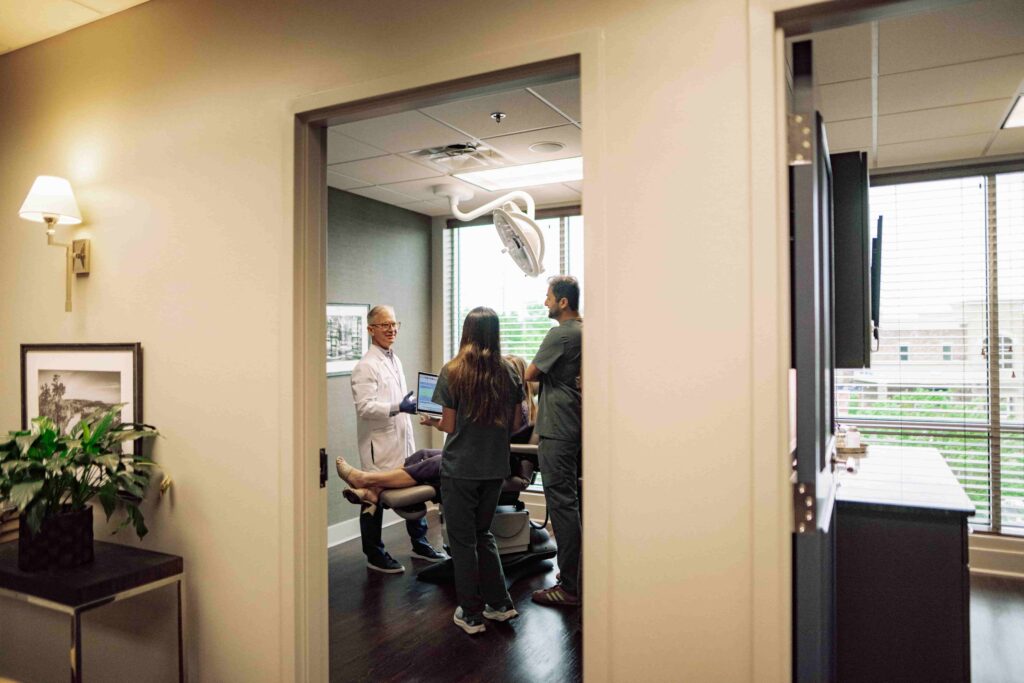 A doctor speaking with two students and a patient in an exam room.