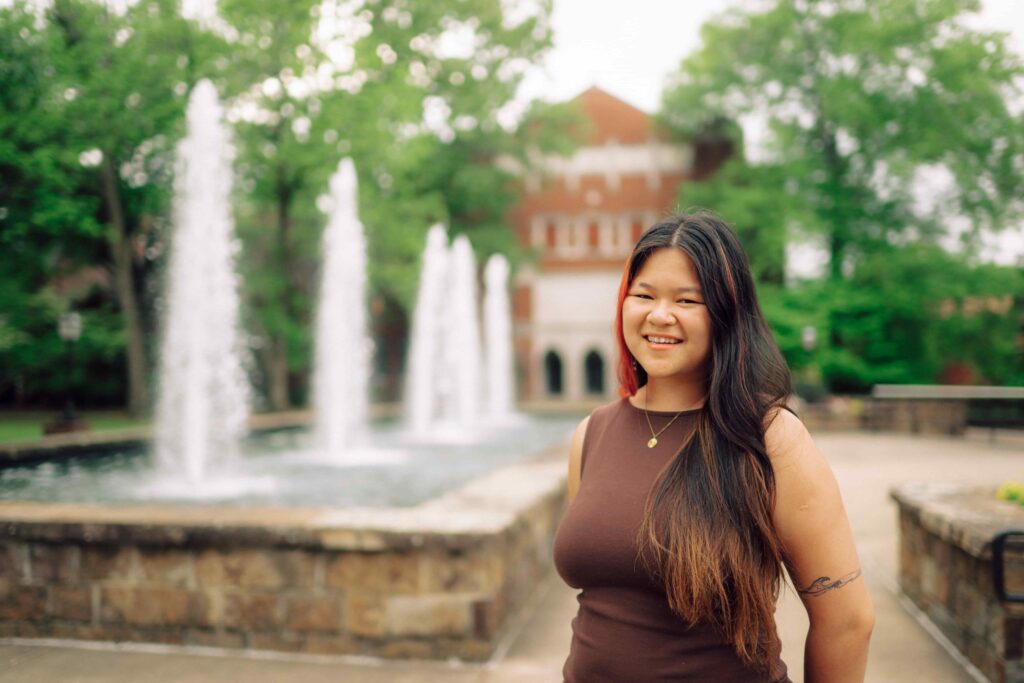 A smiling Hendrix student standing in front of a series of sculptural water fountains on campus.