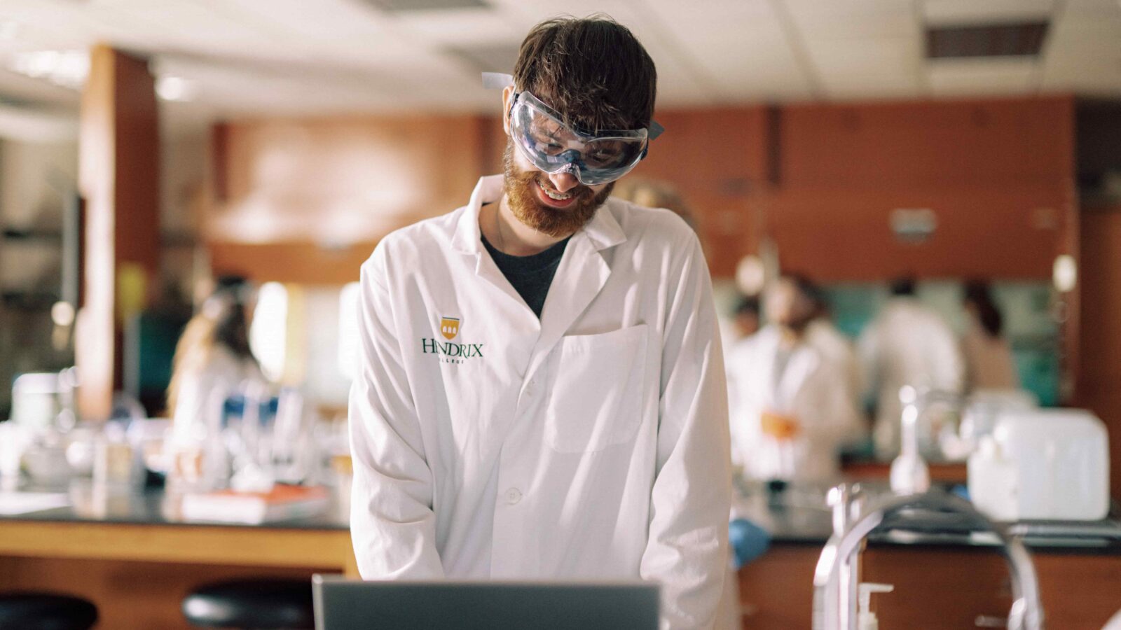 A student wearing safety goggles and a lab coat in a science lab.