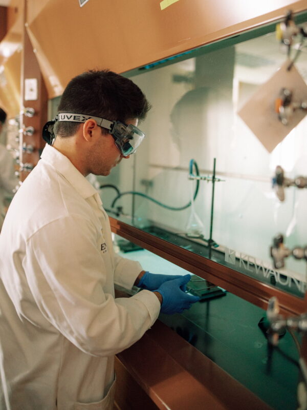 Hendrix College biology student wearing a lab coat, goggles, and gloves works inside a laboratory fume hood.