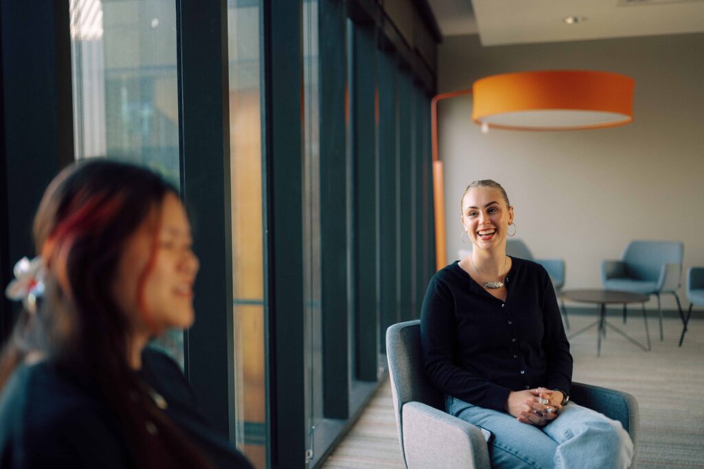 Two seated students having a conversation in a lounge area.