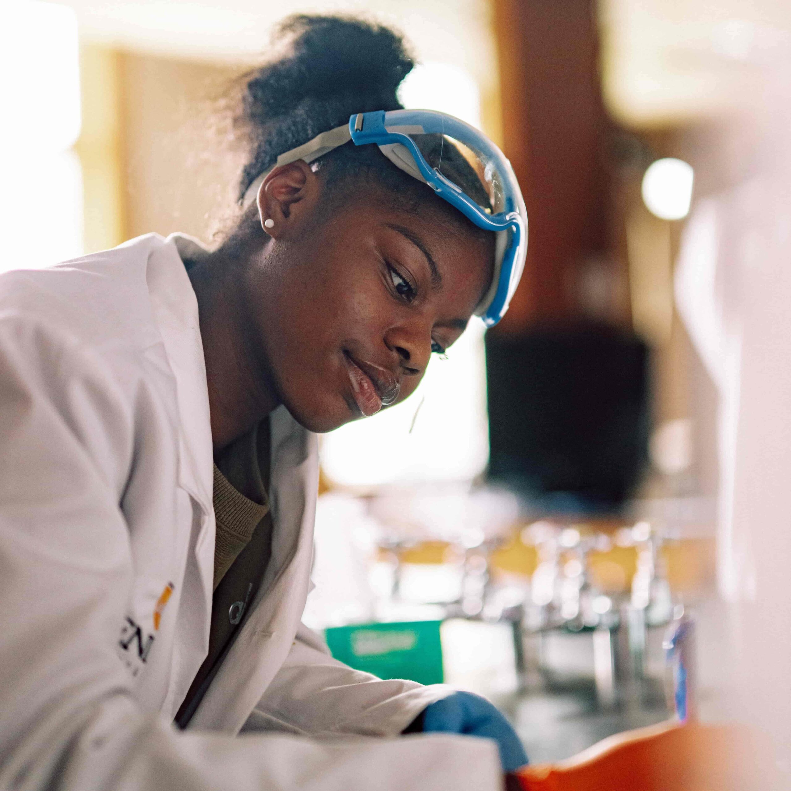 A student wearing safety gear writing notes about an experiment in a science lab.