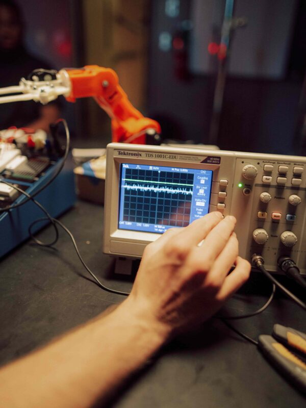 A hand adjusting the settings on an oscilloscope in an electronics lab.