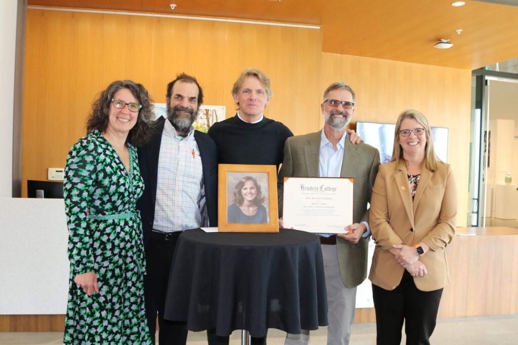 A group of five people standing by a small table. One is holding a certificate to celebrate a scholarship.