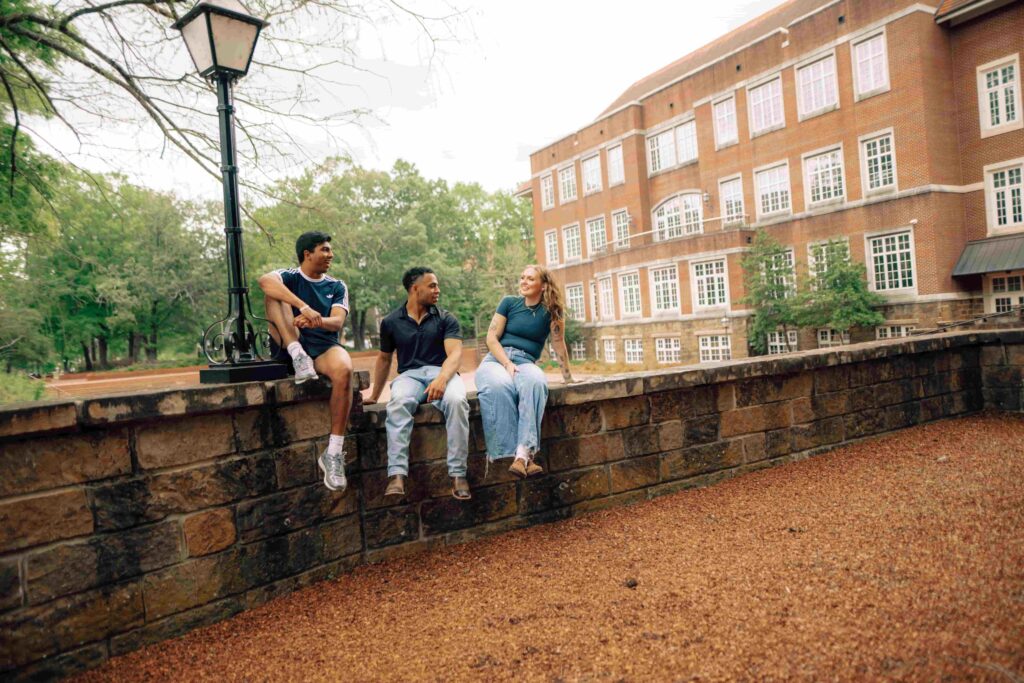 Three Hendrix students sitting on a stone wall on campus.