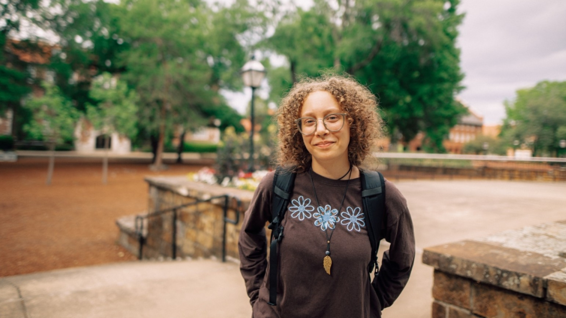 One Hendrix student smiles, wearing a backpack near the steps outside on a sunny day.