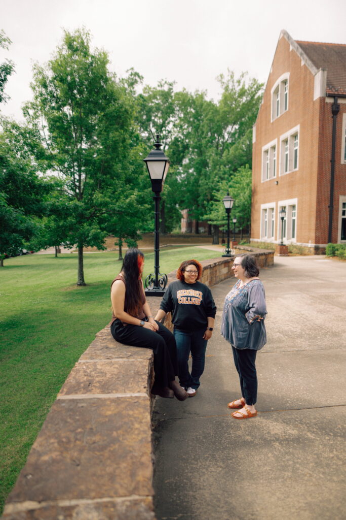 A Hendrix staff member speaking to two students near a stone wall on the Hendrix campus.