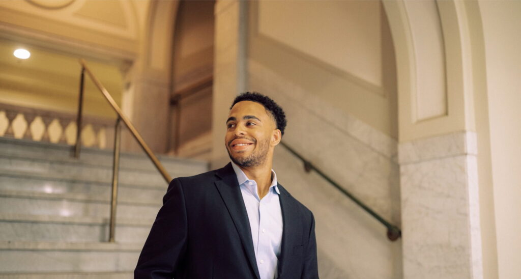 Smiling Hendrix alumnus standing on steps leading into a formal building lobby.