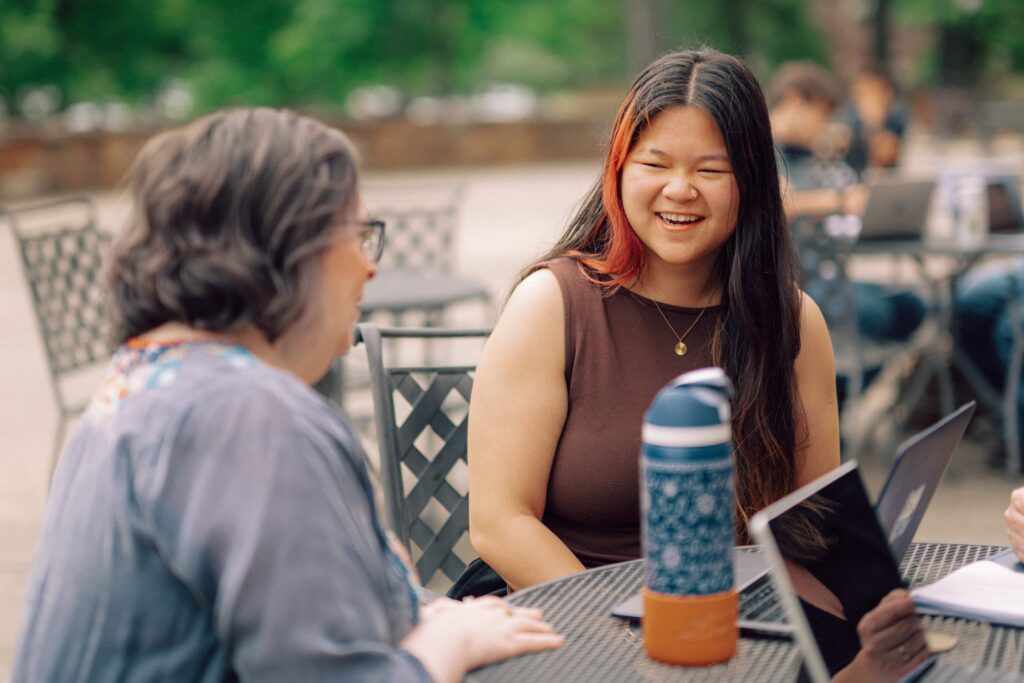 A faculty member and a student having a conversation at an outdoor table.