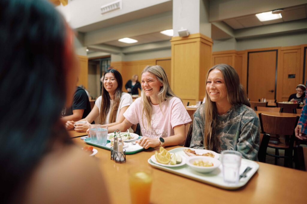 Students with trays of food, eating a meal in a campus dining facility.