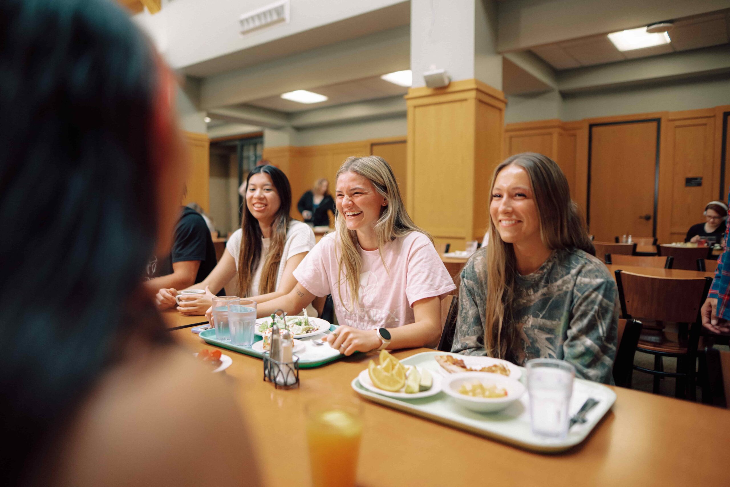 Students with trays of food, eating a meal in a campus dining facility.