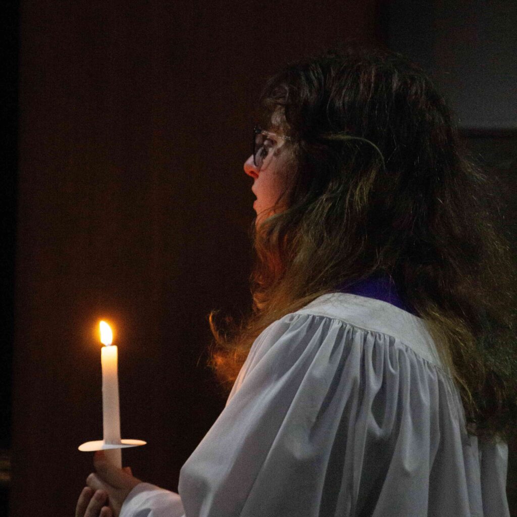 A student holding a lit candle during a religious service.