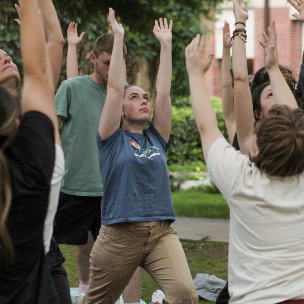 A group of students practicing yoga outdoors on campus.