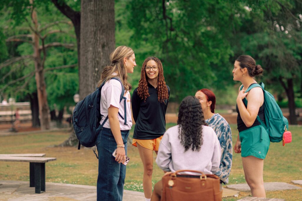 A group of five students having a conversation outdoors on campus.