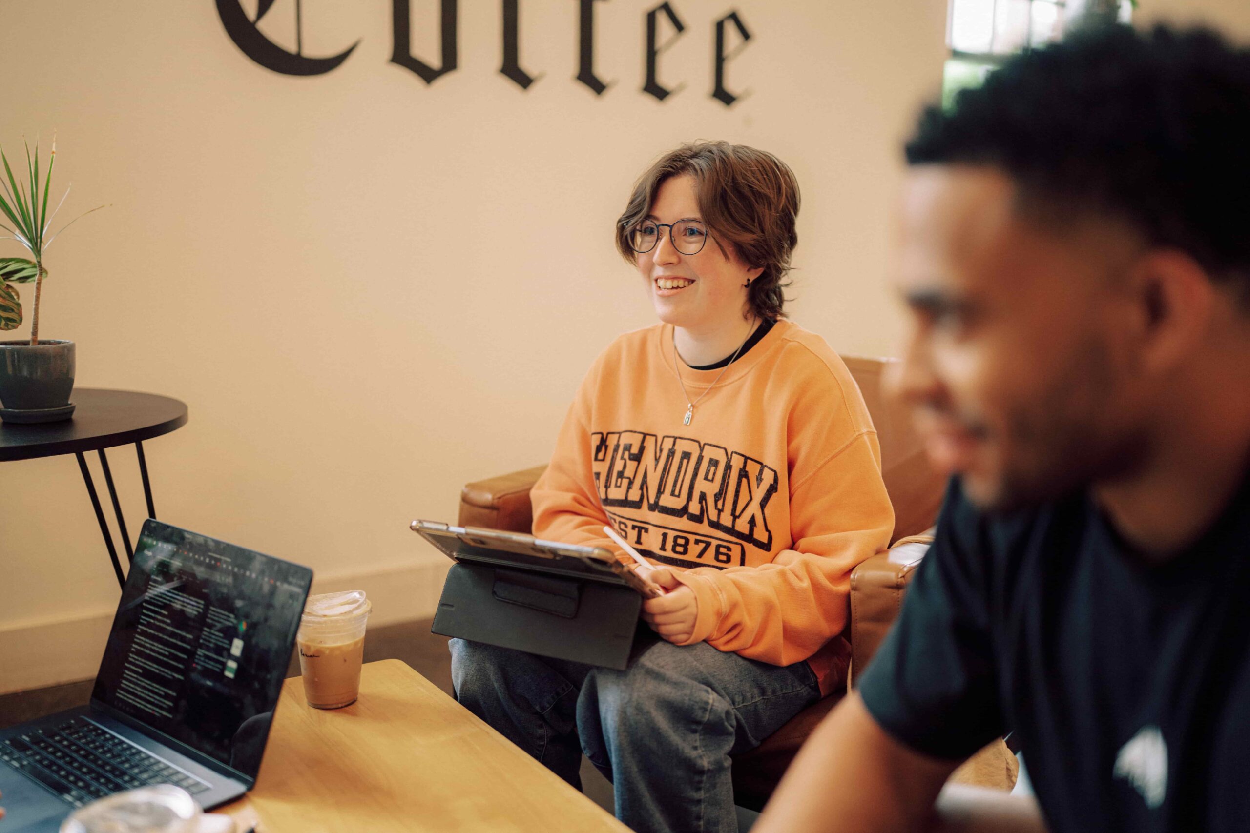 A group of students sitting in a coffee shop with laptops and other electronics.